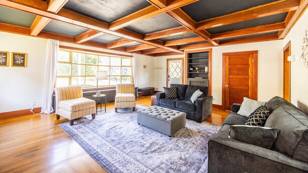 A spacious living room with wooden beams, a fireplace, and a large window.