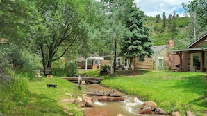 A rustic cabin with a small stream flowing through a grassy area.