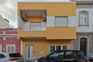 Un immeuble de deux étages avec une façade jaune, un balcon orné de climatiseurs et une porte de garage.