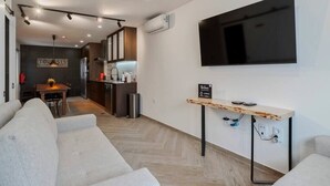 Un salon moderne avec un canapé, un téléviseur fixé au mur et une petite table sur laquelle est posé un panneau.