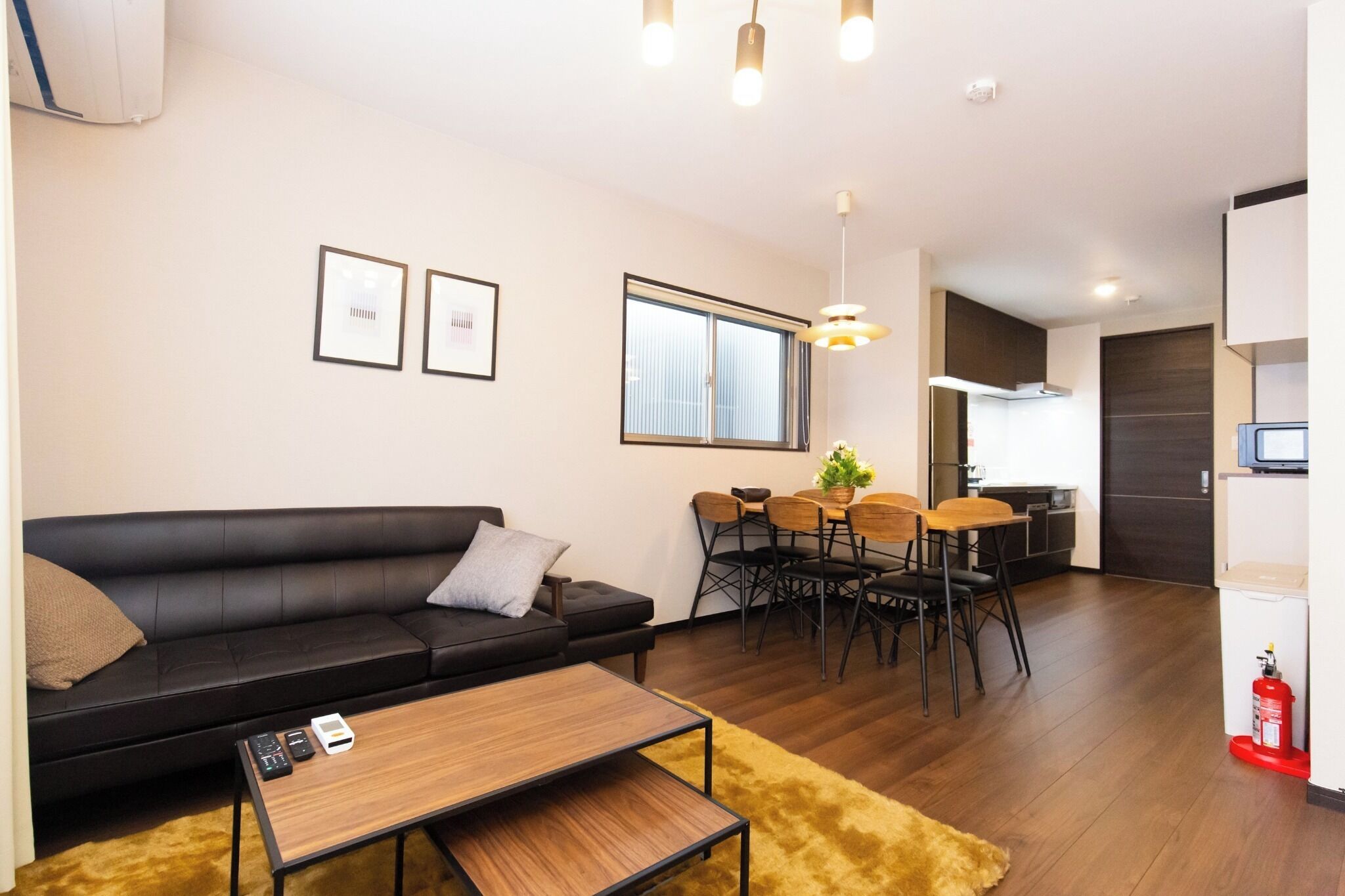 A modern living room with a black leather sofa, a wooden coffee table, and a dining area with a table and chairs.