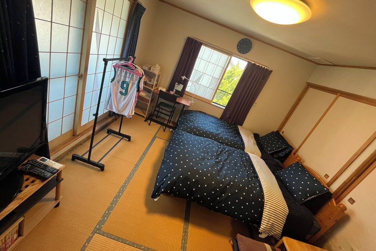 Une pièce de style japonais traditionnel, avec un sol recouvert de tatamis, un futon servant de lit, une télévision et un porte-vêtements.