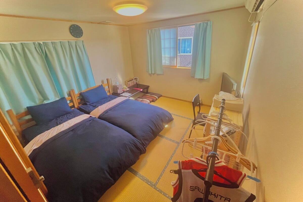 Une chambre d’hôtel avec deux lits, une petite table, une fenêtre avec des rideaux et une table de chevet avec une lampe.