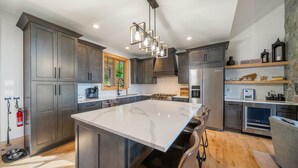 Une cuisine moderne avec des meubles de couleur sombre, un grand îlot central et des appareils électroménagers en acier inoxydable.
