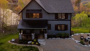 Une maison à deux étages, dotée d’un toit en pente, d’un porche à l’avant et offrant une vue sur un paysage montagneux.