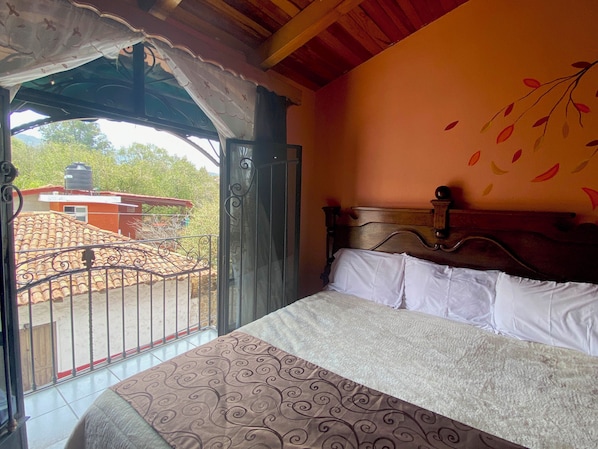A bedroom with a bed, a window with a view of a red-roofed building, and a decorative wall mural.