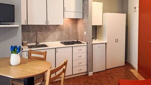 A compact kitchen with white cabinets, a gas stove, and a sink. There is a dining table with chairs and a vase of flowers. - Moschettieri by Interhome (Bibione)