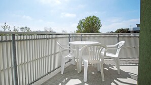A balcony with a white table and chairs, a metal railing, and a view of trees and buildings. - Moschettieri by Interhome (Bibione)