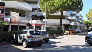 A multi-story building with balconies, parked cars, and a tree in front. - Moschettieri by Interhome (Bibione)