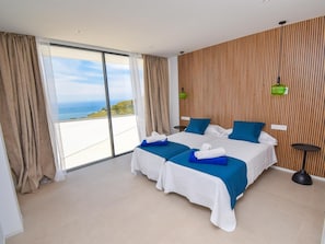 A hotel room with two beds, a large sliding glass door to the balcony, and a wooden panel wall.
