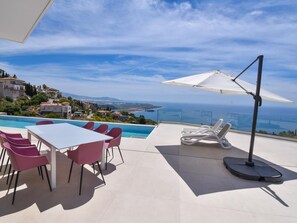 A terrace with a pool, dining area, and lounge chairs with an ocean view.