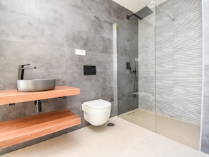 A modern bathroom with a grey tiled wall, a wooden vanity with a sink, a toilet, and a glass shower enclosure.
