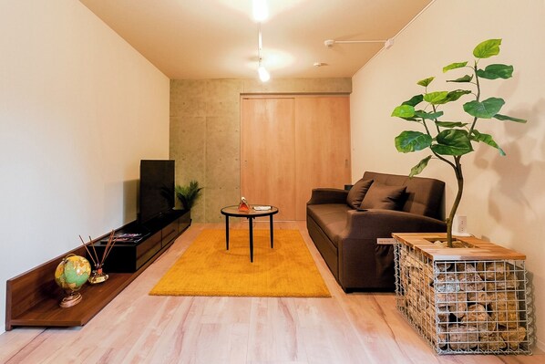 A modern living room with a sofa, a coffee table, a TV, a plant, and a wooden crate.