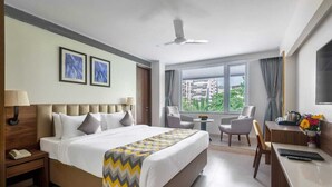 A hotel room with a large bed, a desk, a chair, a small table, and a window with a city view. - Sapphire Boutique Hotel (Navi Mumbai)