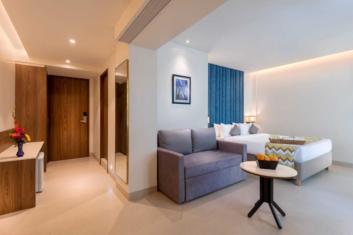 Quarto de hotel moderno com sofá, cama, mesinha e escrivaninha com um vaso de flores.