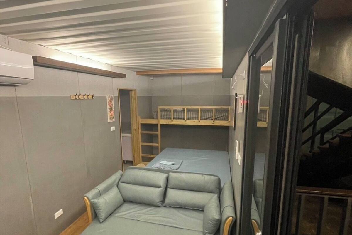 Quarto pequeno com uma cama de solteiro, uma mesinha e uma cama beliche.
