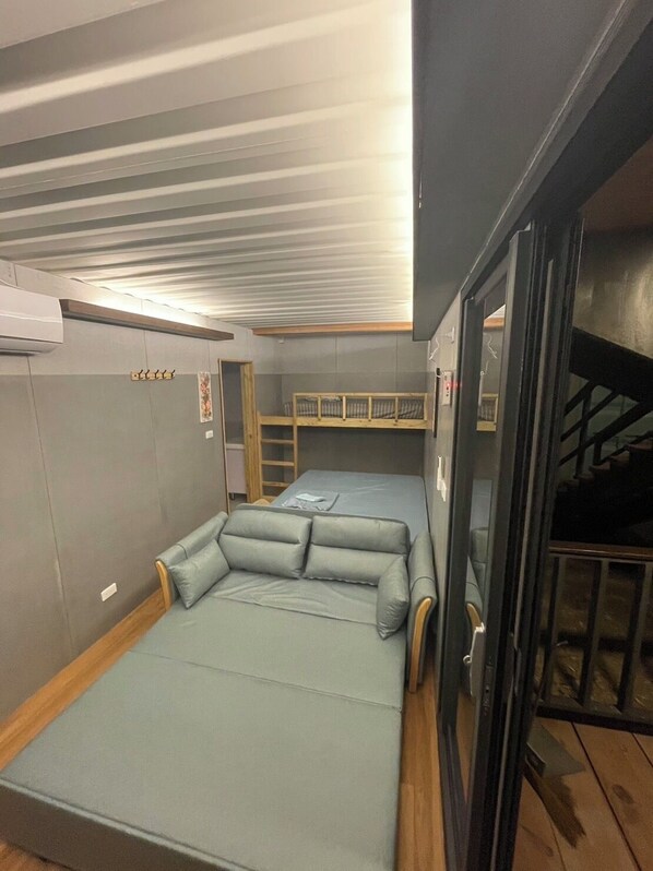 Una habitación pequeña con una cama individual, una mesita y una cama litera.