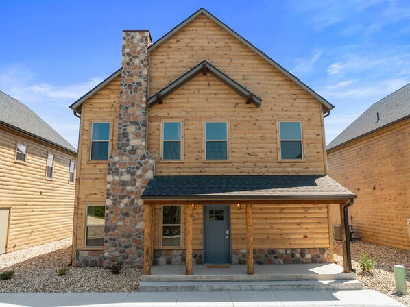 A two-story log cabin with a stone chimney, a front porch, and a small front yard.