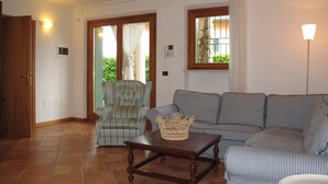 Un soggiorno con un divano a righe, un tavolino in legno, un cesto di vimini, una poltrona a quadri e una porta che dà su un balcone.