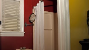 Une salle de bain avec un lavabo blanc, des toilettes, un rideau de douche et une fenêtre avec des stores.