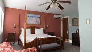 A four-poster bed with a wooden headboard, a ceiling fan, and a painting on the wall.