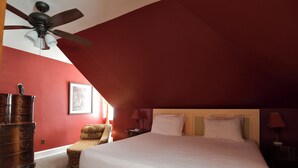 Une chambre à coucher avec un grand lit, une commode en bois, une chaise, un bureau et un ventilateur de plafond.