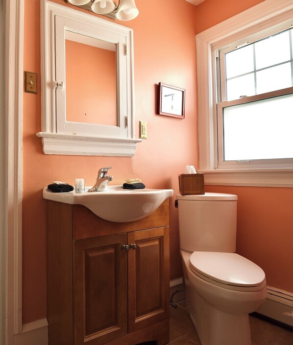 A bathroom with a white sink, wooden cabinets, a white toilet, and a window with blinds.
