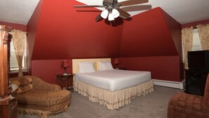 Une chambre à coucher avec un grand lit, un ventilateur de plafond, une chaise en bois et un téléviseur.