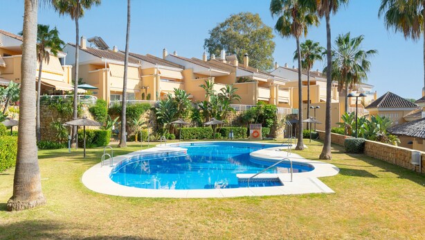 Una piscina envoltada de palmeres i un edifici amb balcons.