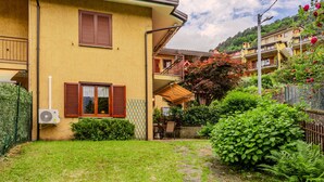 A yellow building with a garden, stone pathway, and a red flowering tree. - Apartment Mofra by Interhome (Bellano)
