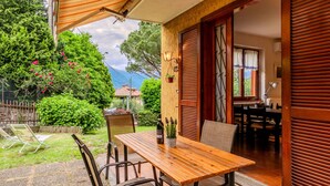 An outdoor patio with a wooden table and chairs, a hanging plant, and a view of a mountain and trees. - Apartment Mofra by Interhome (Bellano)