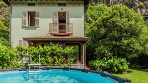 A two-story building with a swimming pool, surrounded by lush greenery and a mountainous backdrop. - La Rina by Interhome (Dervio)