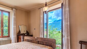 A bedroom with a bed, a nightstand, a dresser, a chair, and a large window with curtains. - La Rina by Interhome (Dervio)