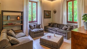 A living room with a sofa set, a coffee table, a bookshelf, and large windows with curtains. - La Rina by Interhome (Dervio)