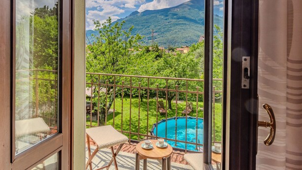 A balcony with a view of a mountain, a swimming pool, and a table with cups. - La Rina by Interhome (Dervio)