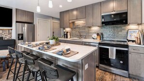 A modern kitchen with a central island, stainless steel appliances, and bar stools. - Gorgeous Condo With River View - Pool and Hot Tub (Bend)