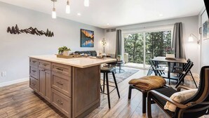 A modern kitchen with a central island, bar stools, and a dining area with a view. - Gorgeous Condo With River View - Pool and Hot Tub (Bend)