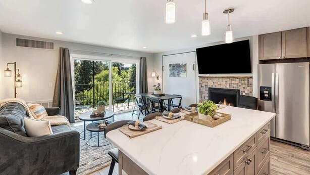 A modern kitchen with a large island, a dining area with outdoor seating, and a fireplace. - Gorgeous Condo With River View - Pool and Hot Tub (Bend)