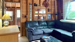 A cozy cabin interior with a leather sofa, wooden walls, a town line sign, and a lobster sign. - Historic 1940s lakeside cabin on  spring-fed pond. Close to Acadia National Park (Franklin)