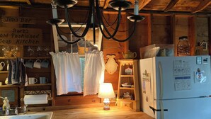 A rustic kitchen with wooden cabinets, a white sink, a chandelier, and a refrigerator with magnets and papers. - Historic 1940s lakeside cabin on  spring-fed pond. Close to Acadia National Park (Franklin)