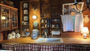 A rustic kitchen with wooden cabinets, a coffee maker, and a sink. There are various kitchen utensils and a sign that reads "Jim's Bar Barb's 01d Fashioned Soup Kitchen". - Historic 1940s lakeside cabin on  spring-fed pond. Close to Acadia National Park (Franklin)