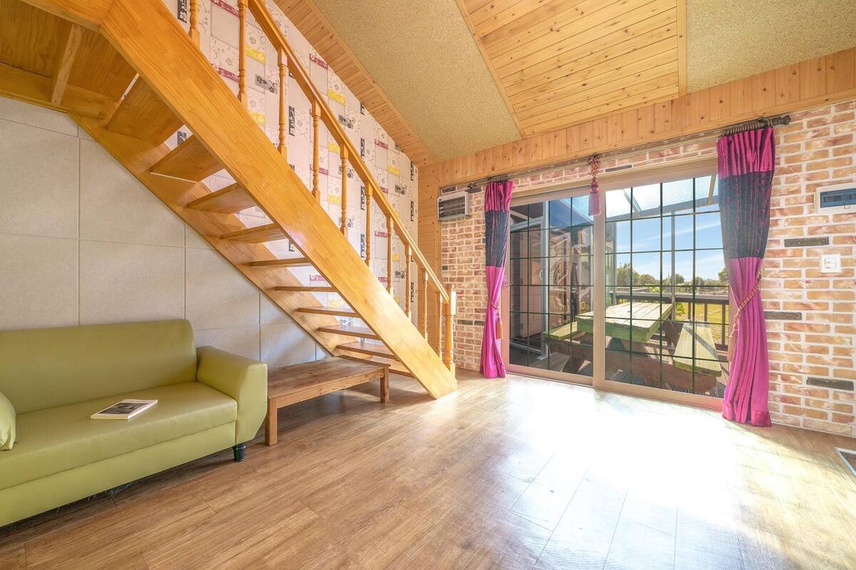 Een kamer met een houten trap, een groene bank en een groot raam met gordijnen.