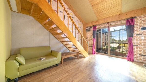 Een kamer met een houten trap, een groene bank en een groot raam met gordijnen.