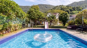 Une piscine avec un flotteur en forme de cœur, entourée de verdure et offrant une vue sur des maisons au loin.