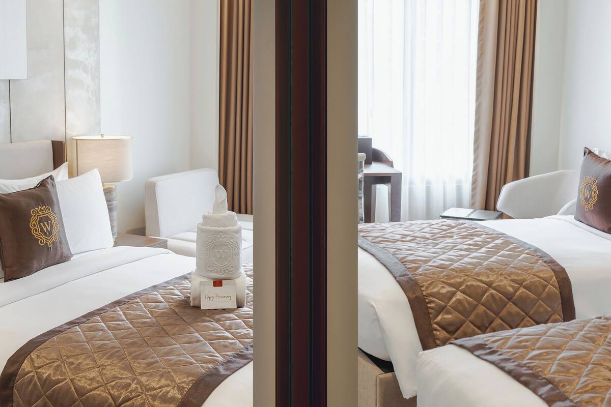 A hotel room with two beds, a sitting area, and a view of the outdoors.