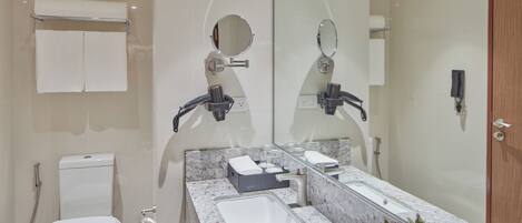 A modern bathroom with a marble sink, a large mirror, a toilet, and a shower.