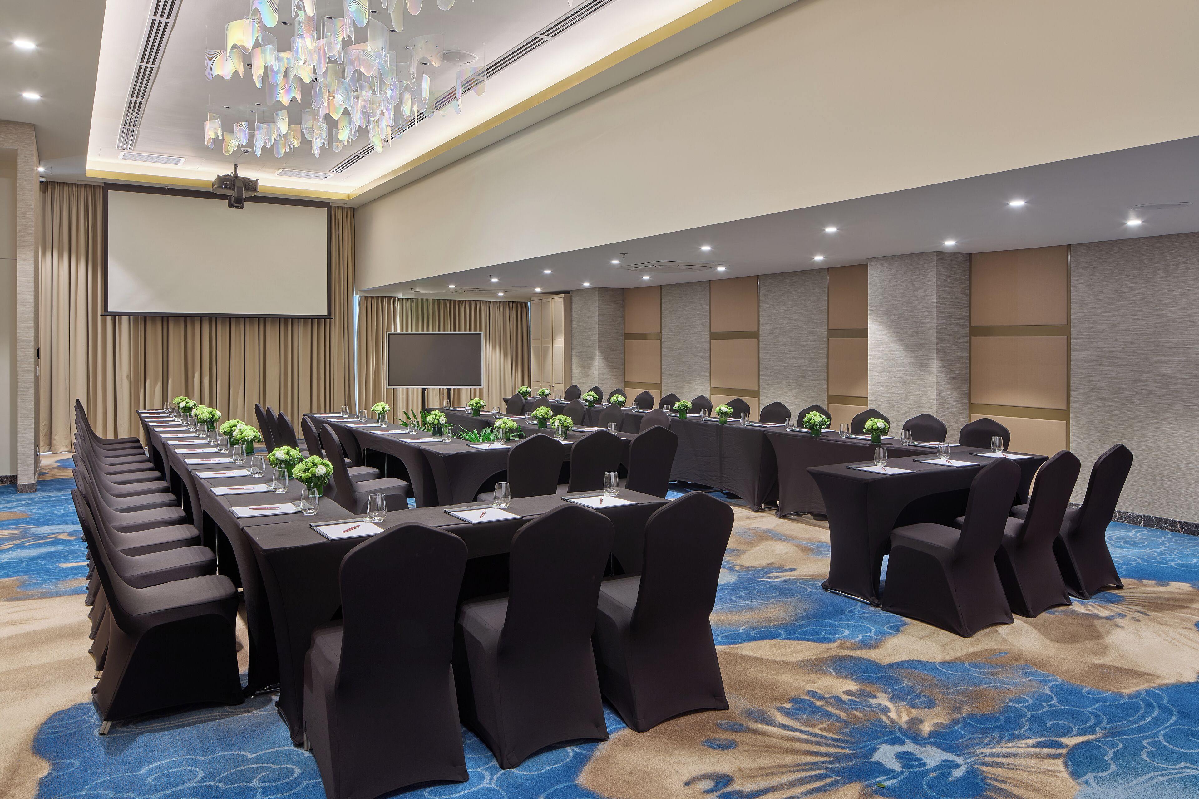 A conference room with long tables, black chairs, and a large screen.