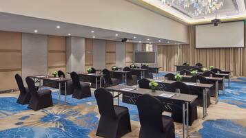 A conference room with tables, chairs, a large screen, and a carpeted floor.