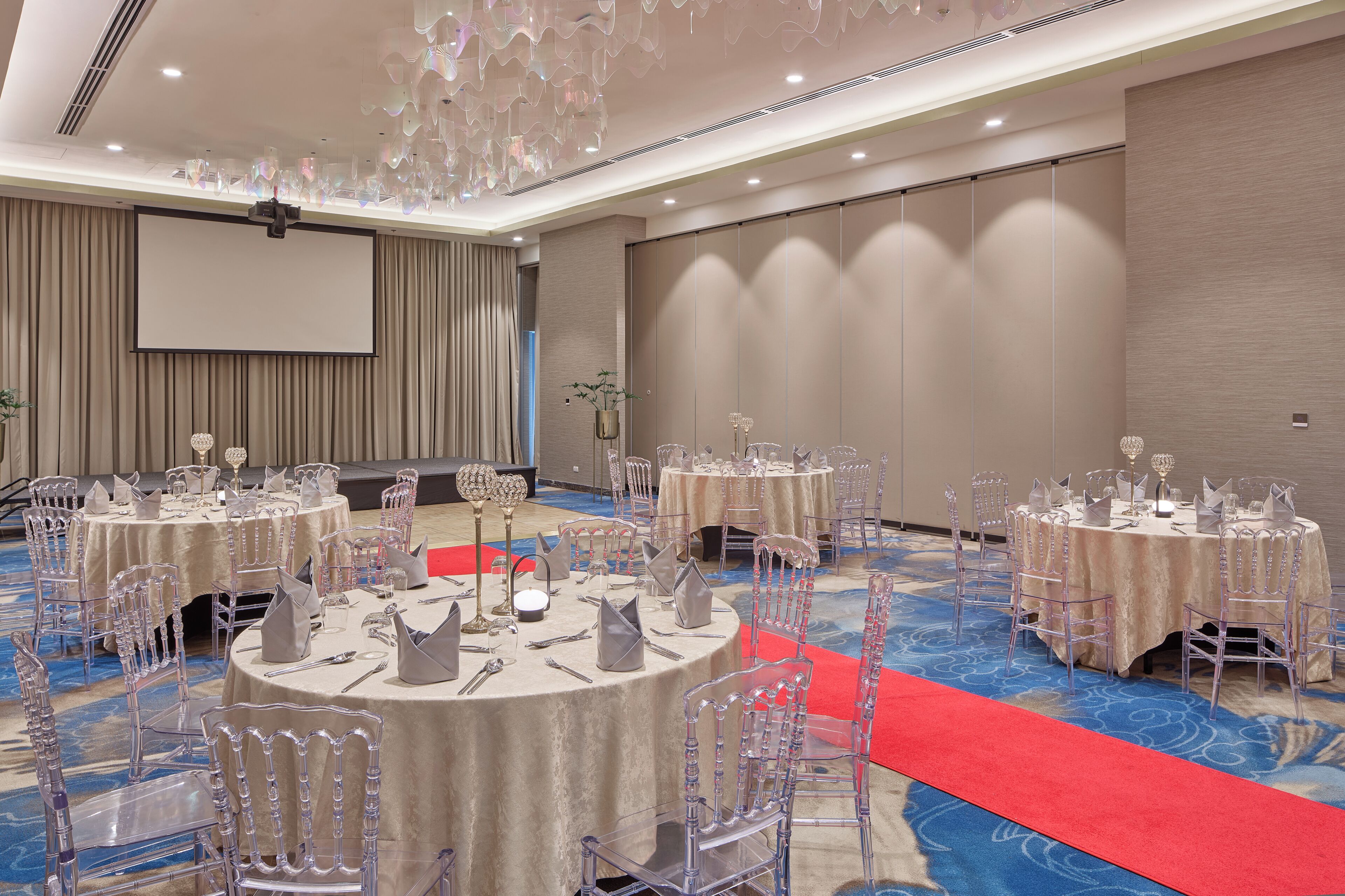 A banquet hall with round tables, clear chairs, and a red carpet.