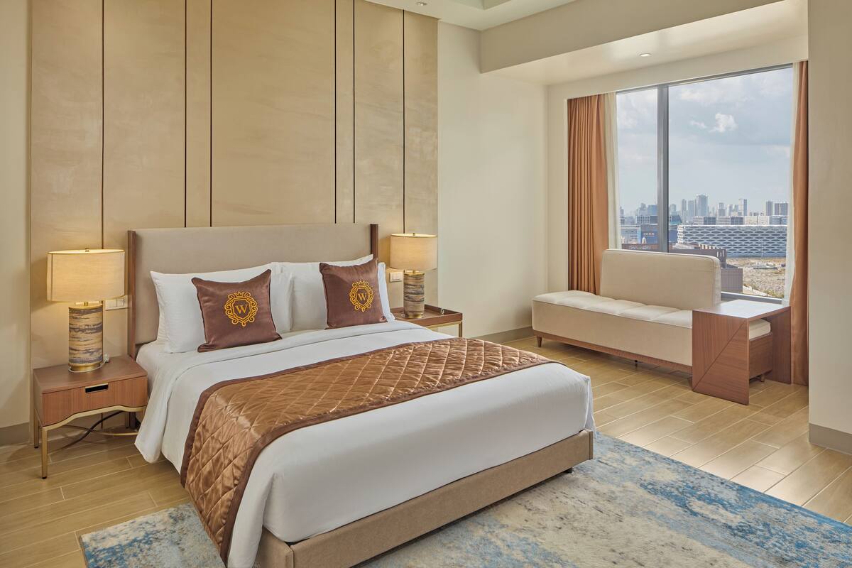 A modern hotel room with a large bed, a seating area, and a city view.